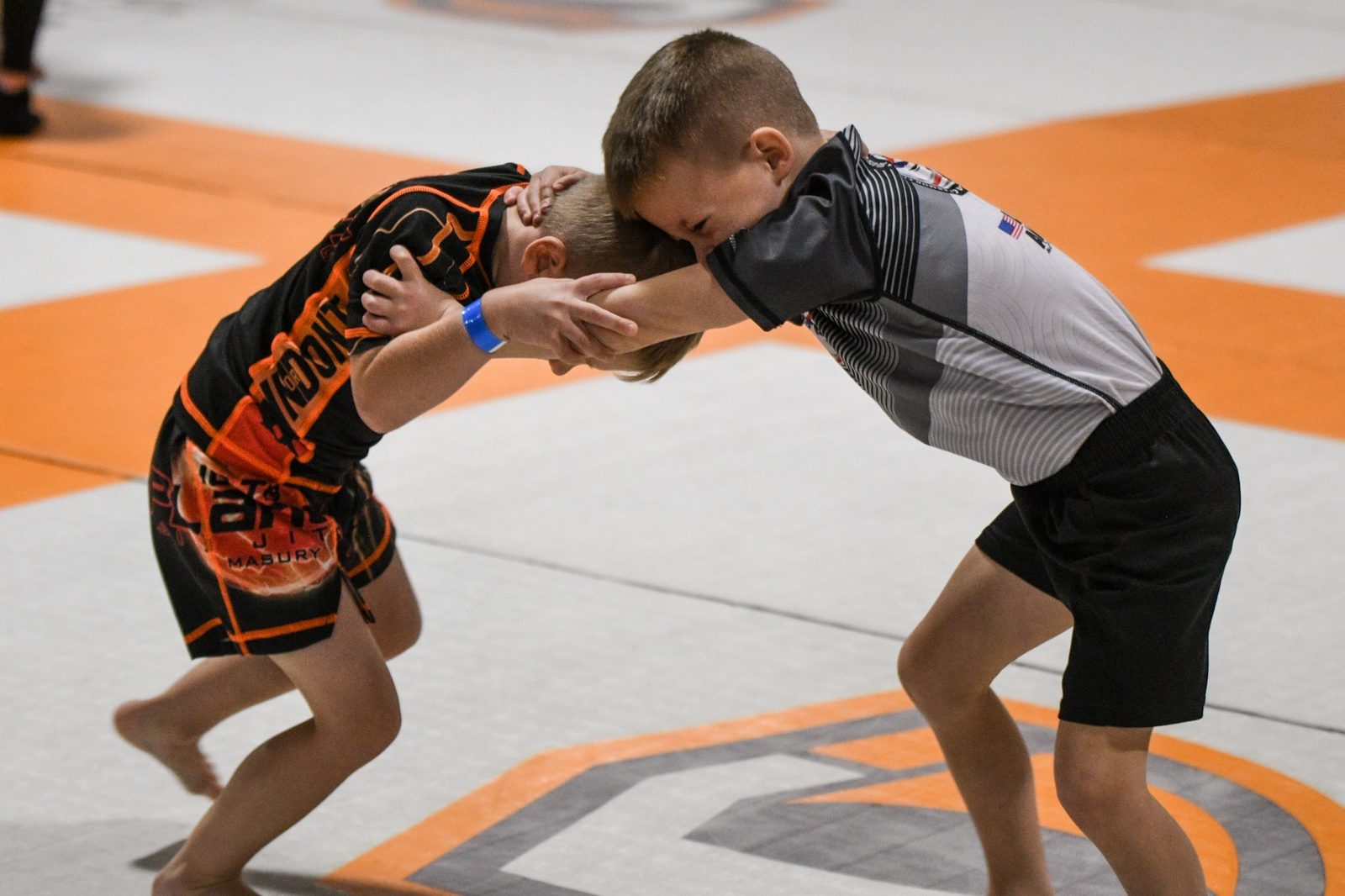 Two young grapplers in a clinch at a no-gi tournament, one in 10th Planet Masury shorts