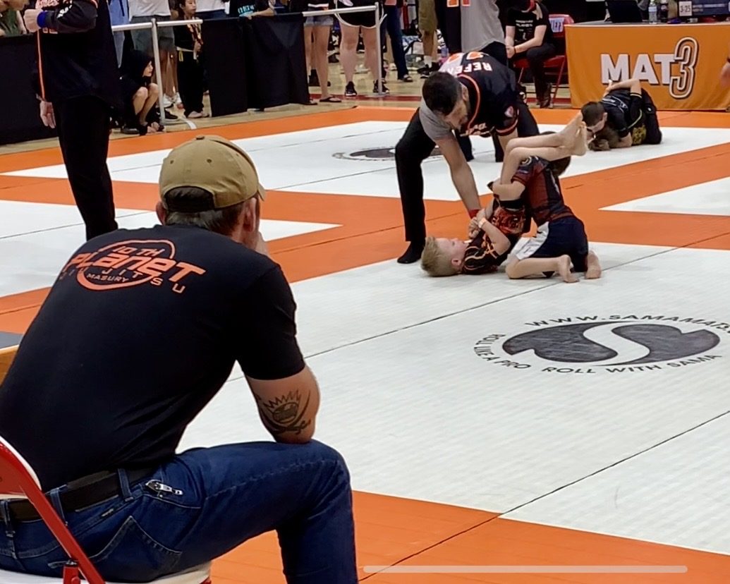 A 10th Planet Masury coach watching from the corner while two kids compete